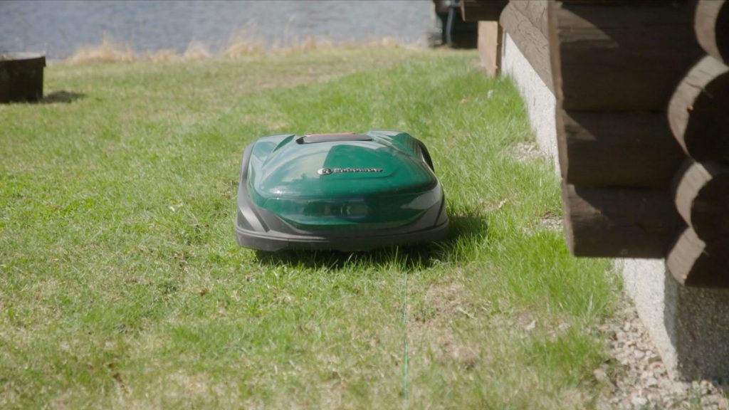 Robottiruohonleikkuri leikkaa nurmikkoa talon vierellä.